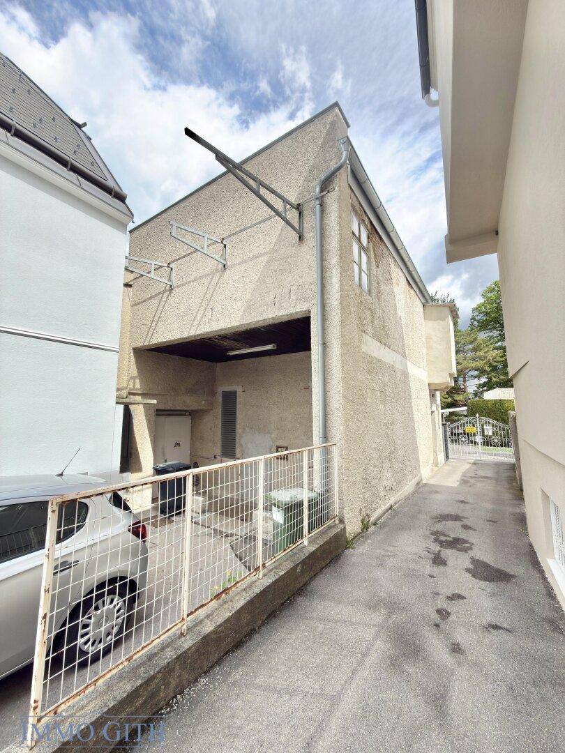 Seitenansicht eines Gebäudes mit Zufahrt, geparktem Auto und einfacher Fassade.