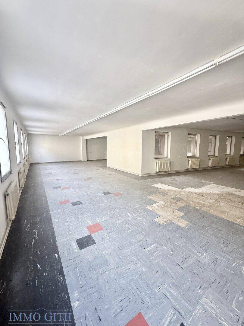 Langer, offener Raum mit Reihen von Fenstern und einem gemusterten Bodenbelag, unrenoviert.