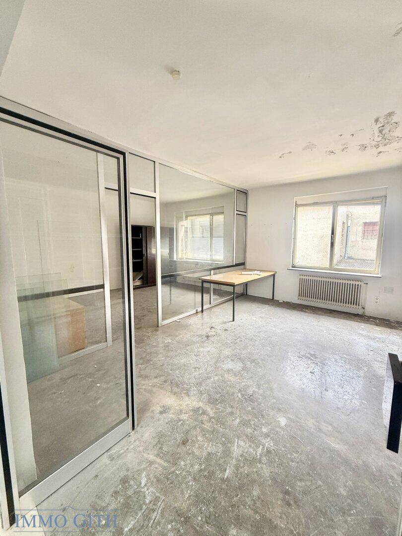 Heller Raum mit Glaswänden, einem Tisch und abgenutztem Betonboden, ideal für ein Büro.