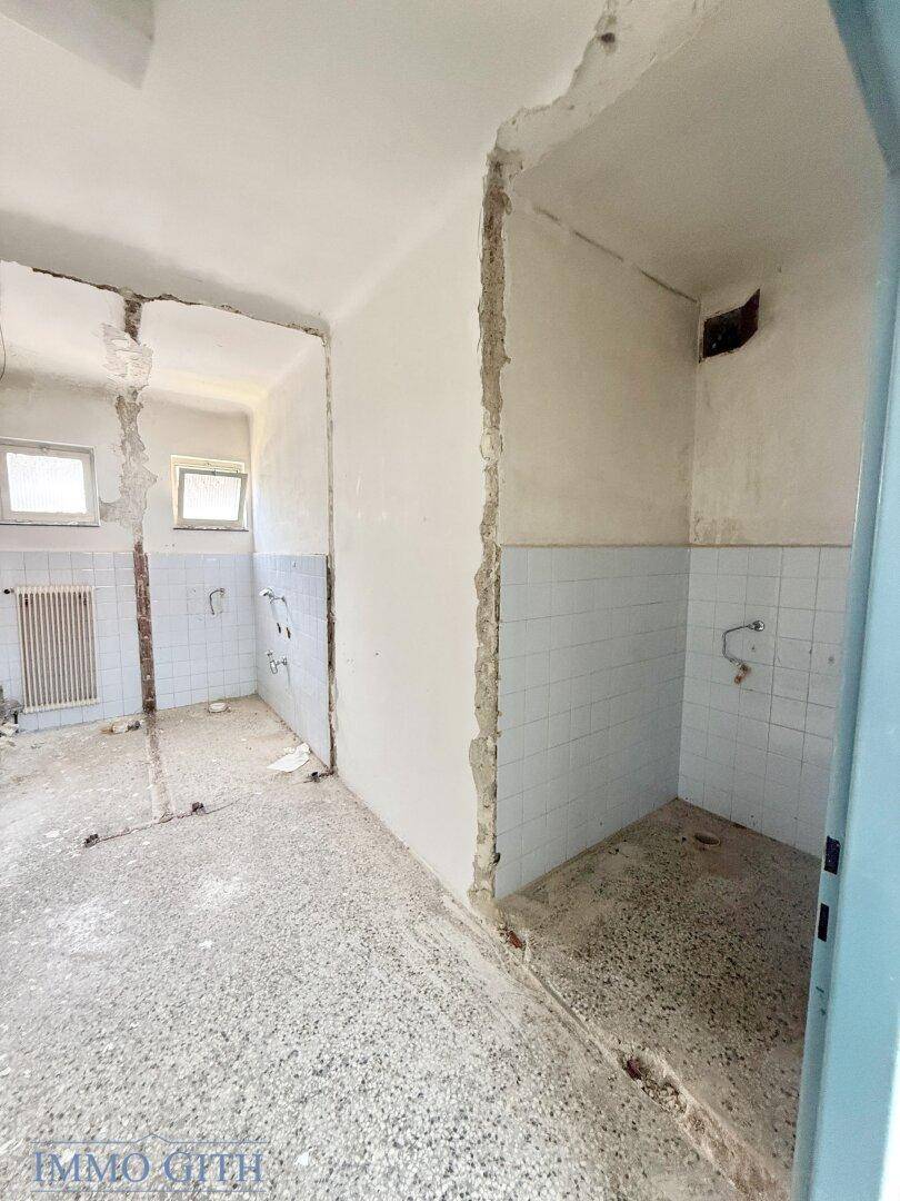 Unfertiges Badezimmer mit blauen Fliesen und einer Duschkabine im Rohbau, renovierungsbedürftig.
