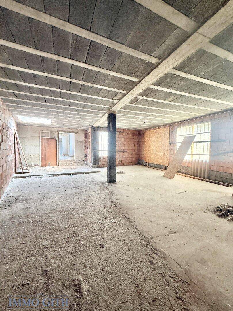 Unfertiger Raum mit unverputzten Ziegelwänden, Betonboden und sichtbaren Deckenbalken.