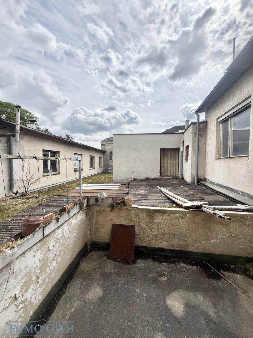 Abgenutzte Dachterrasse mit Blick auf umliegende Gebäude und den Himmel, renovierungsbedürftig.