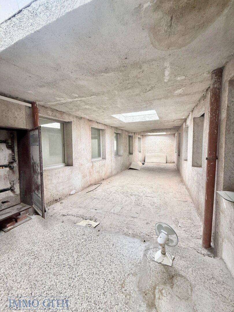 Langer, schmaler Raum mit Fenstern, Betonboden und einem Ventilator, unfertig.