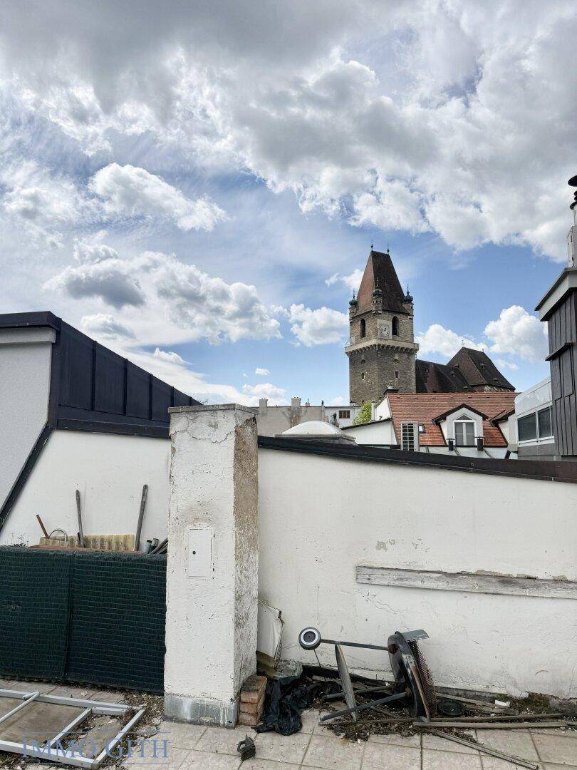 Blick von einer vernachlässigten Dachterrasse mit Fliesenboden auf einen historischen Turm und die Umgebung.