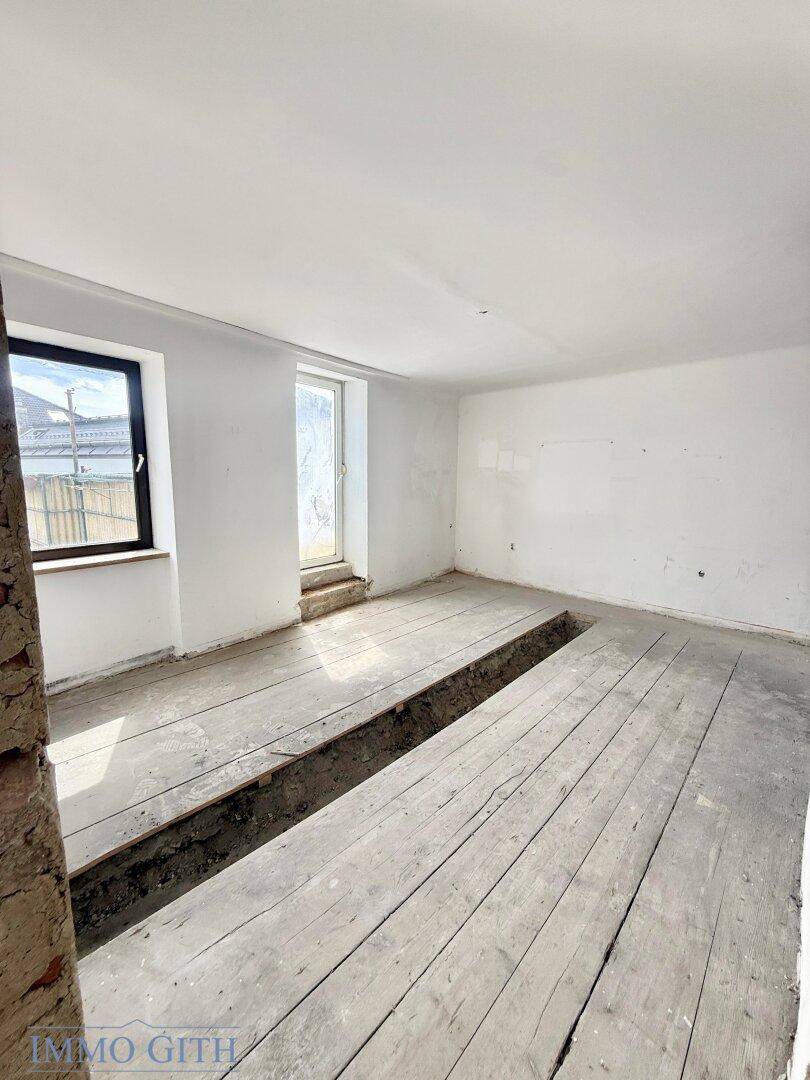 Innenraum im Rohbauzustand mit freigelegten Holzdielen und einem Graben für Installationen.