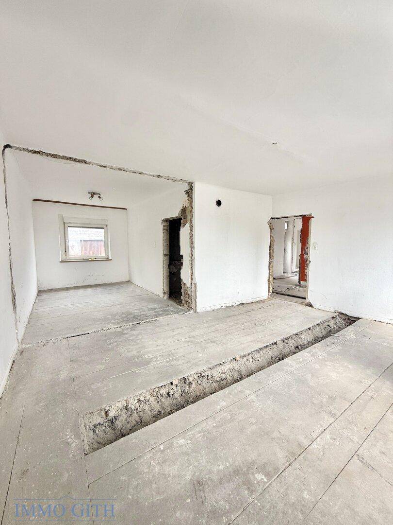 Renovierungsbedürftiger Innenraum mit offenen Wanddurchbrüchen und freigelegten Holzdielen.