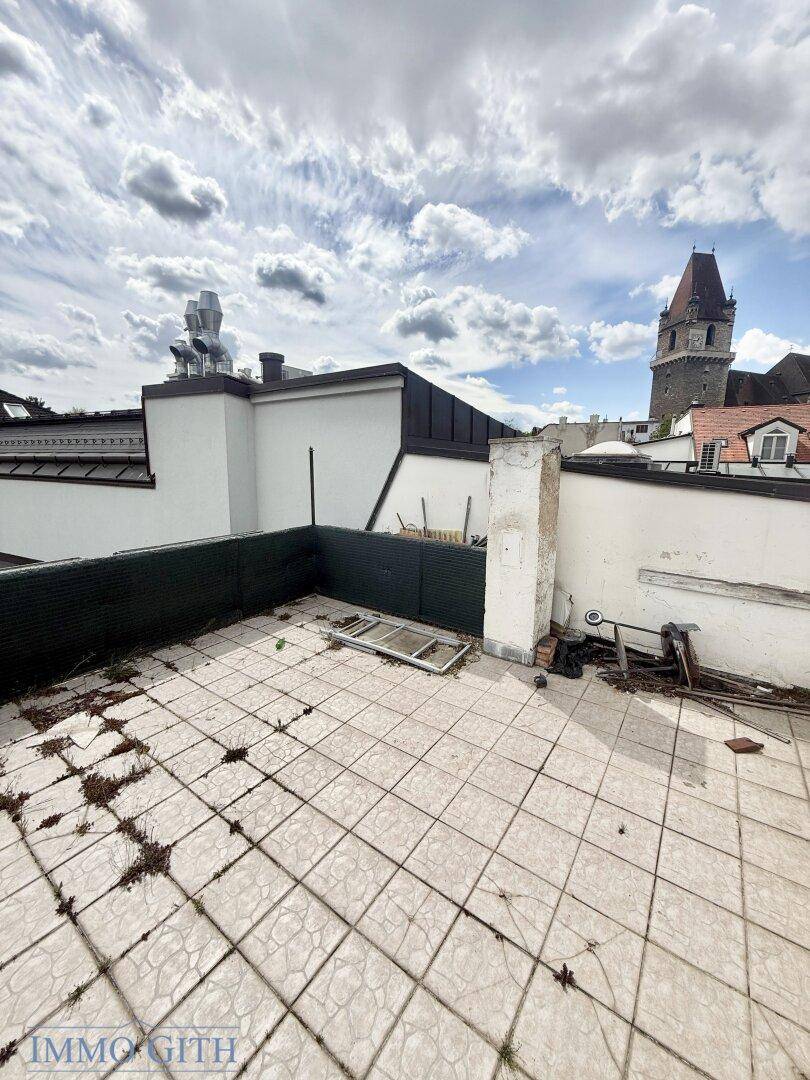 Weitläufige Dachterrasse mit Fliesenboden und Blick auf den historischen Turm und die Stadt.