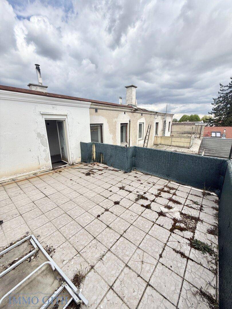 Vernachlässigte Dachterrasse mit Fliesenboden und Blick auf umliegende Gebäude.