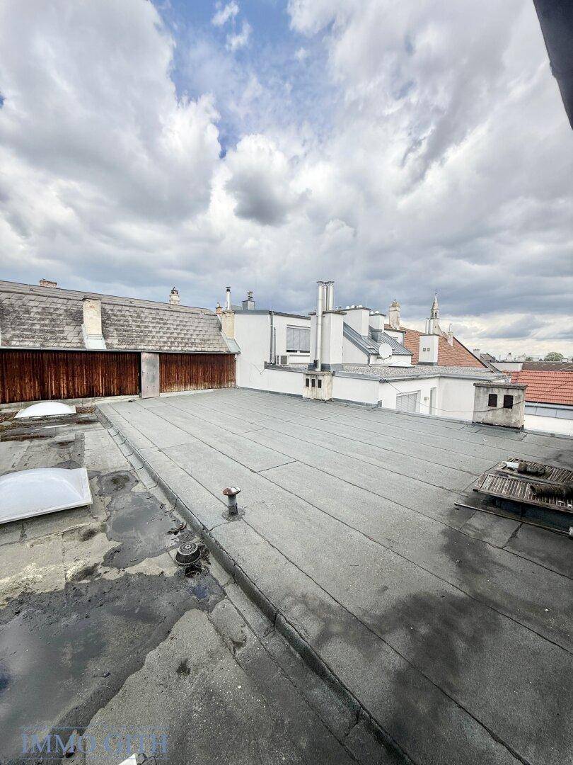 Blick über flache Dächer und angrenzende Gebäude unter einem bewölkten Himmel.