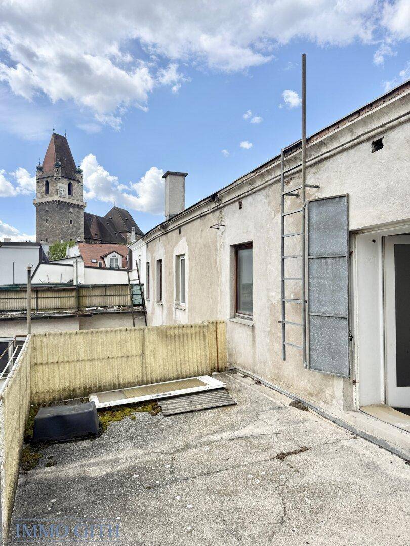 Betonierte Terrasse mit Zugang zum Gebäude und Fernblick auf einen historischen Kirchturm.
