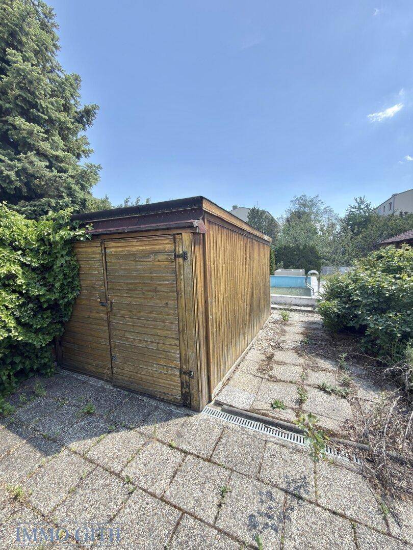 Praktischer Gartenschuppen aus Holz neben einem gepflasterten Bereich im Garten.