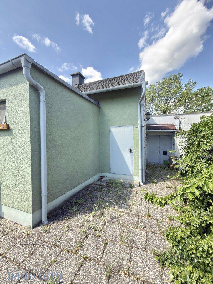 Seitenansicht eines grünen Gebäudes mit gepflastertem Außenbereich und Regenrinne.