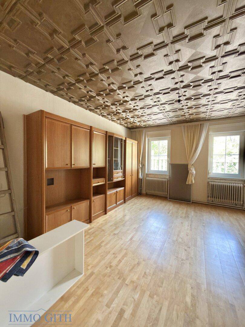 Helles Wohnzimmer mit dekorativer Decke, Parkettboden und großen Fenstern.
