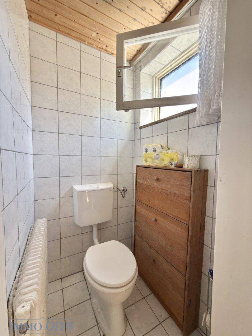 Separates WC mit Toilette, kleinem Holzschrank und Fenster für natürliche Belüftung.