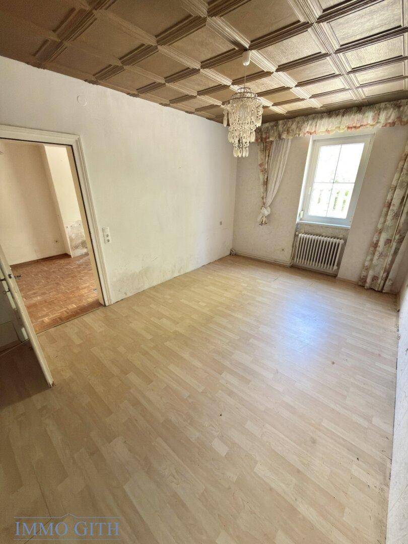 Leeres Zimmer mit Kronleuchter, Parkettboden und Fenster, bereit zur Gestaltung.