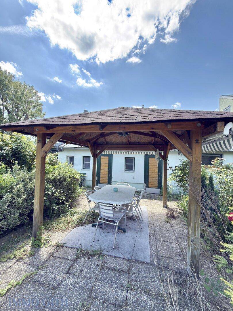 Gemütlicher Gartenpavillon mit Esstisch und Stühlen im Außenbereich, umgeben von Grün.