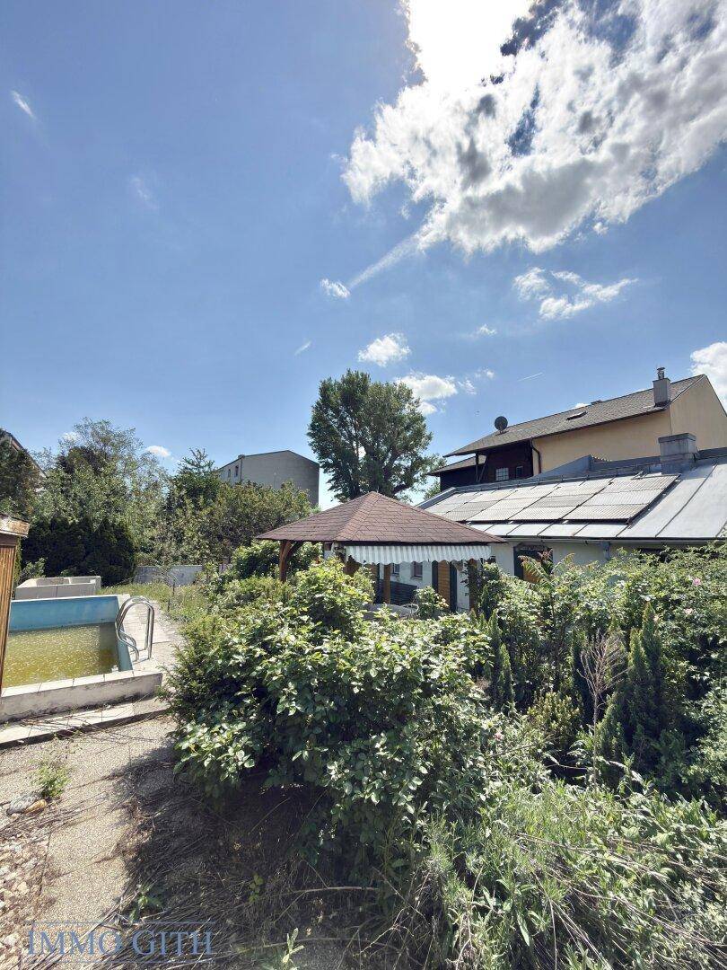 Gesamtansicht des Hauses mit Garten, Pool und Solaranlage auf dem Dach unter blauem Himmel.