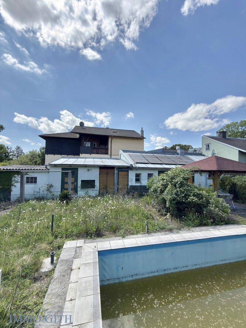 Rückansicht des Hauses mit leerstehendem Pool und verwildertem Gartenbereich, renovierungsbedürftig.