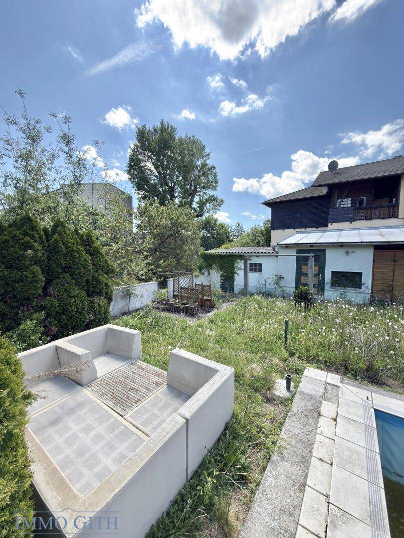 Gartenbereich mit gemauertem Grillplatz und Blick auf den Pool, umgeben von Vegetation.