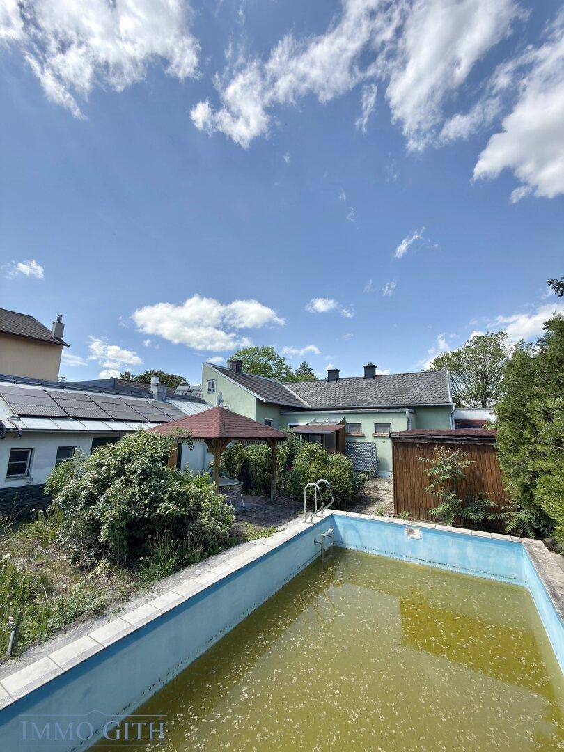 Blick auf den Poolbereich und die Rückseite des Hauses mit Solaranlage und viel Grün.