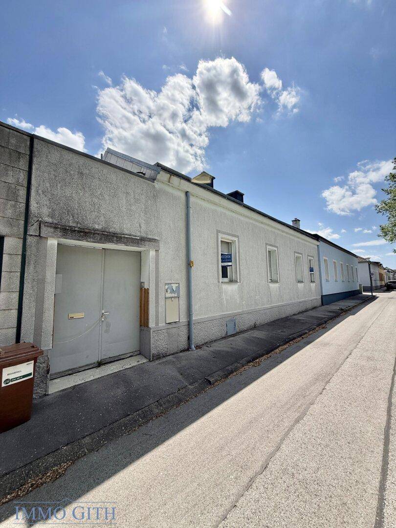 Seitenansicht eines weißen Gebäudes an einer ruhigen Straße mit Mülltonnen.