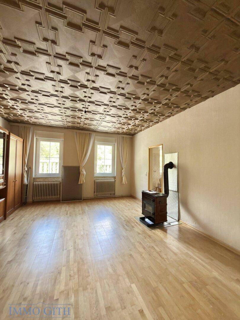 Gemütliches Wohnzimmer mit dekorativer Decke, Holzofen und Parkettboden.