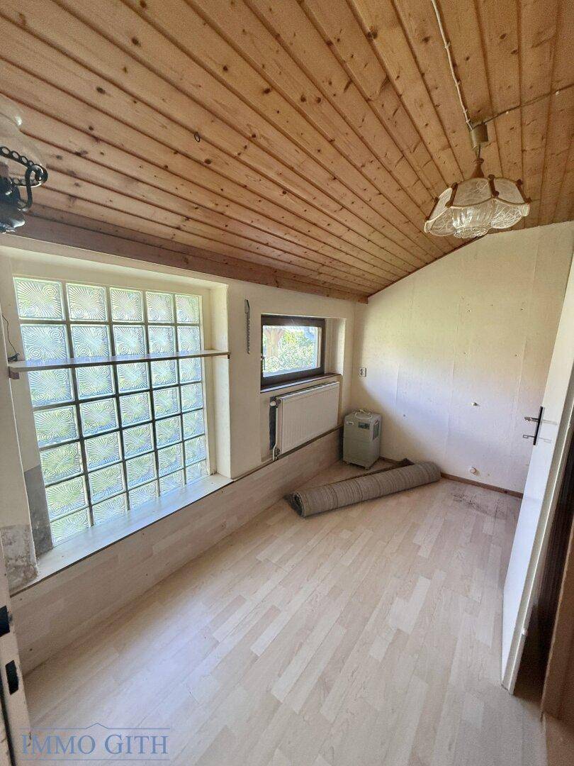 Helles Zimmer mit Holzdecke, Glasbausteinfenster und Heizkörper.