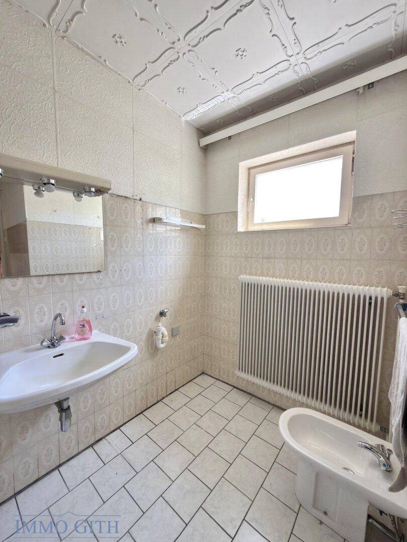 Badezimmer mit Waschbecken, Bidet und Fenster, komplett gefliest in hellem Design.