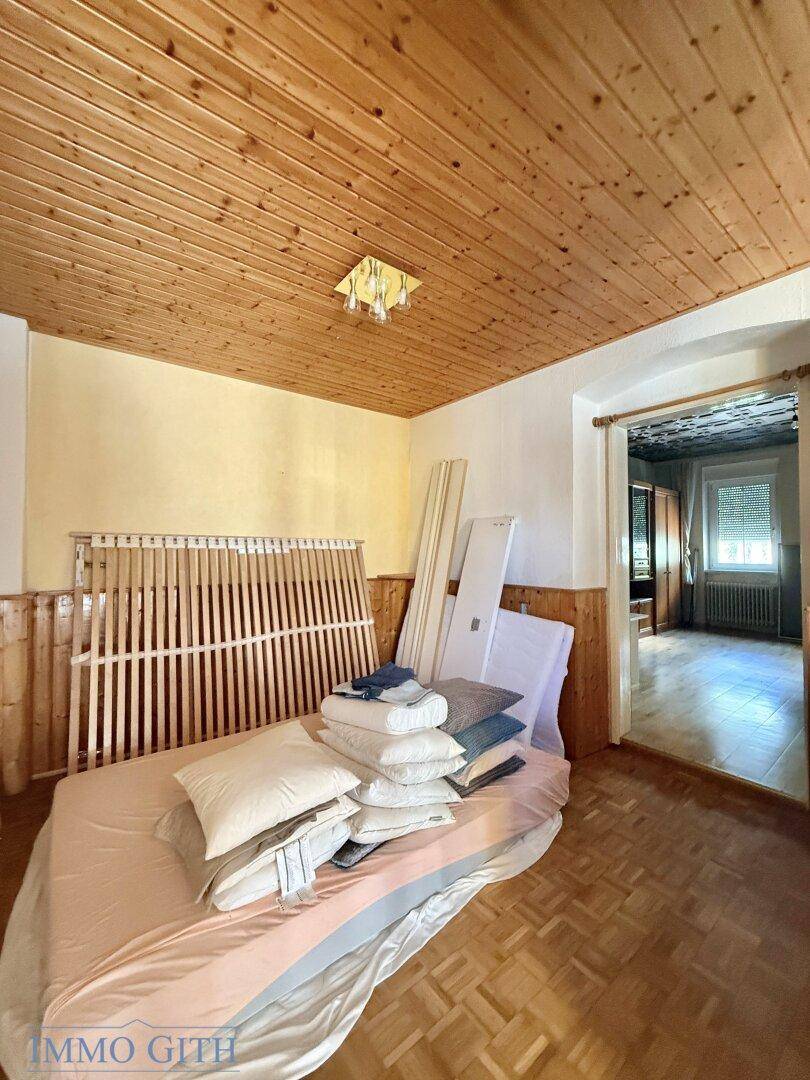 Schlafzimmer mit Holzdecke und Fischgrätparkett, ausgestattet mit einem Bettgestell.