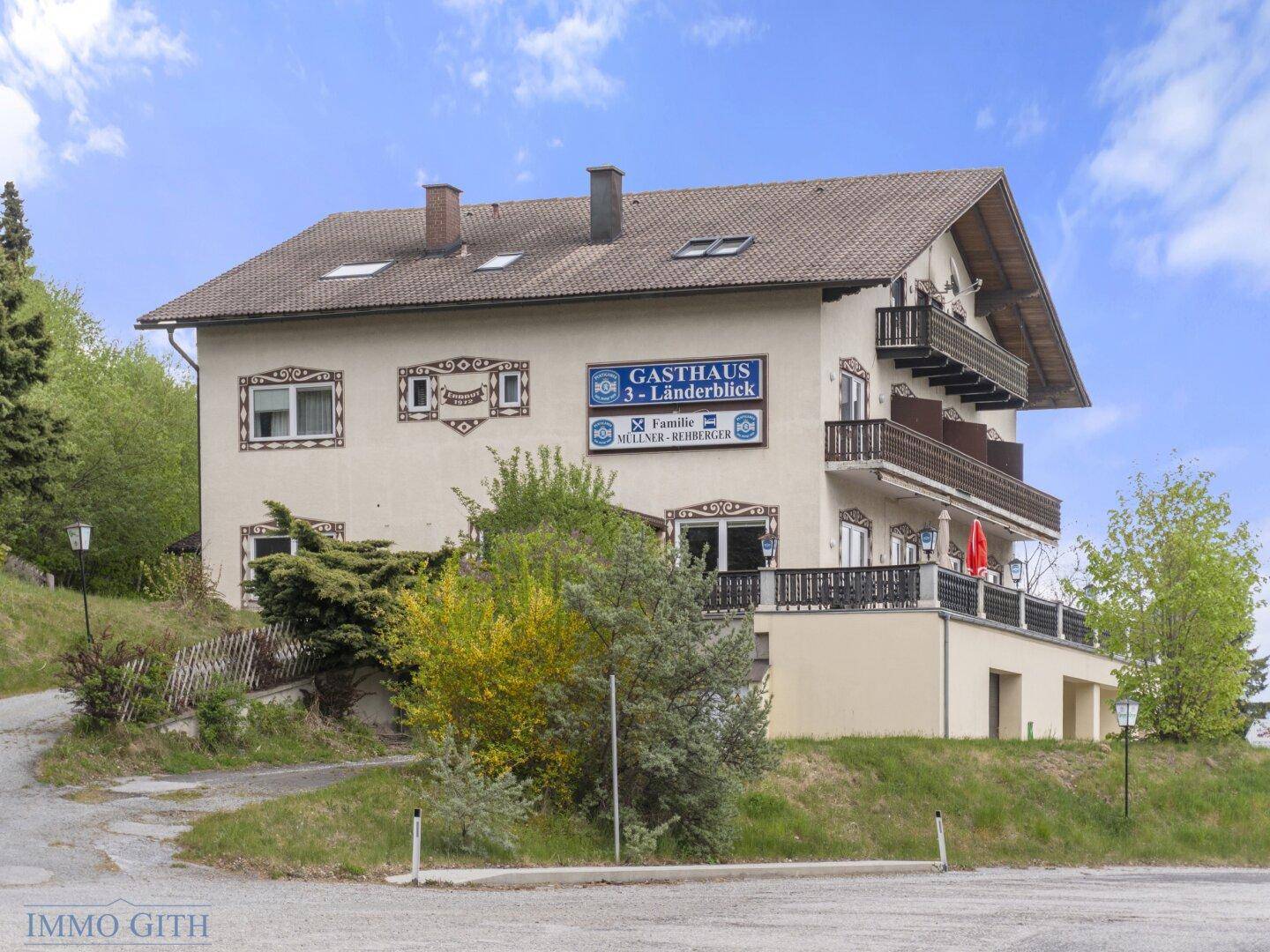 Seitenansicht des Gasthauses mit traditioneller Fassade, Balkonen und einer möblierten Terrasse.