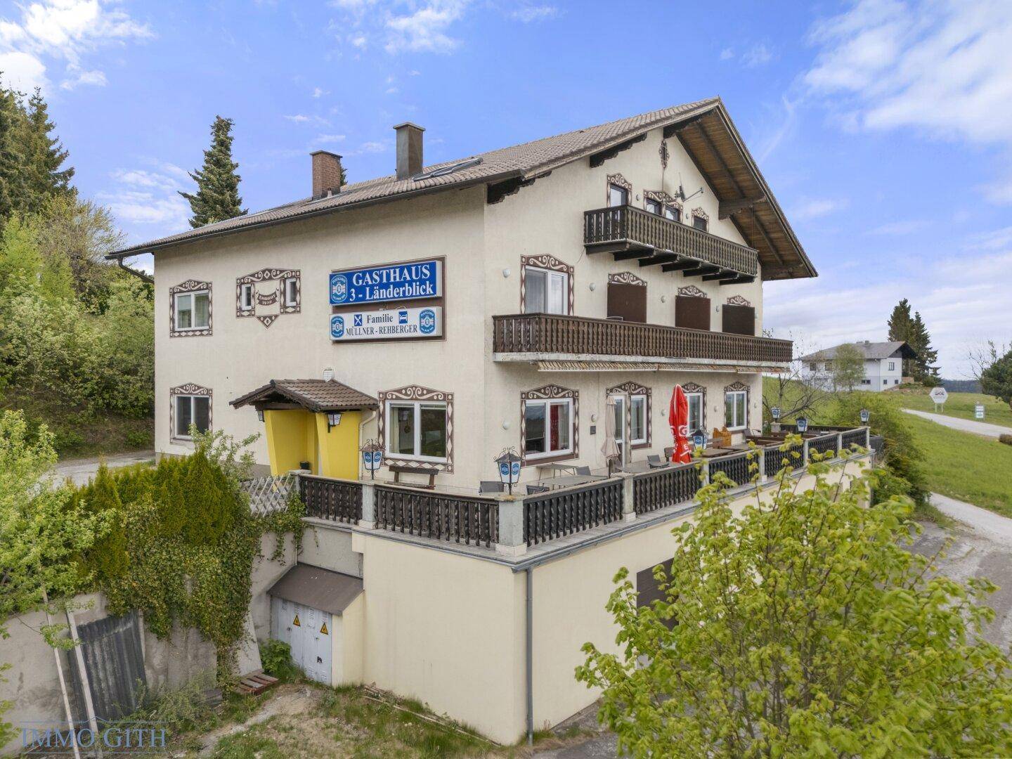 Ansicht des Gasthauses mit traditioneller Architektur, Balkonen und einer großen Terrasse mit Sitzgelegenheiten.