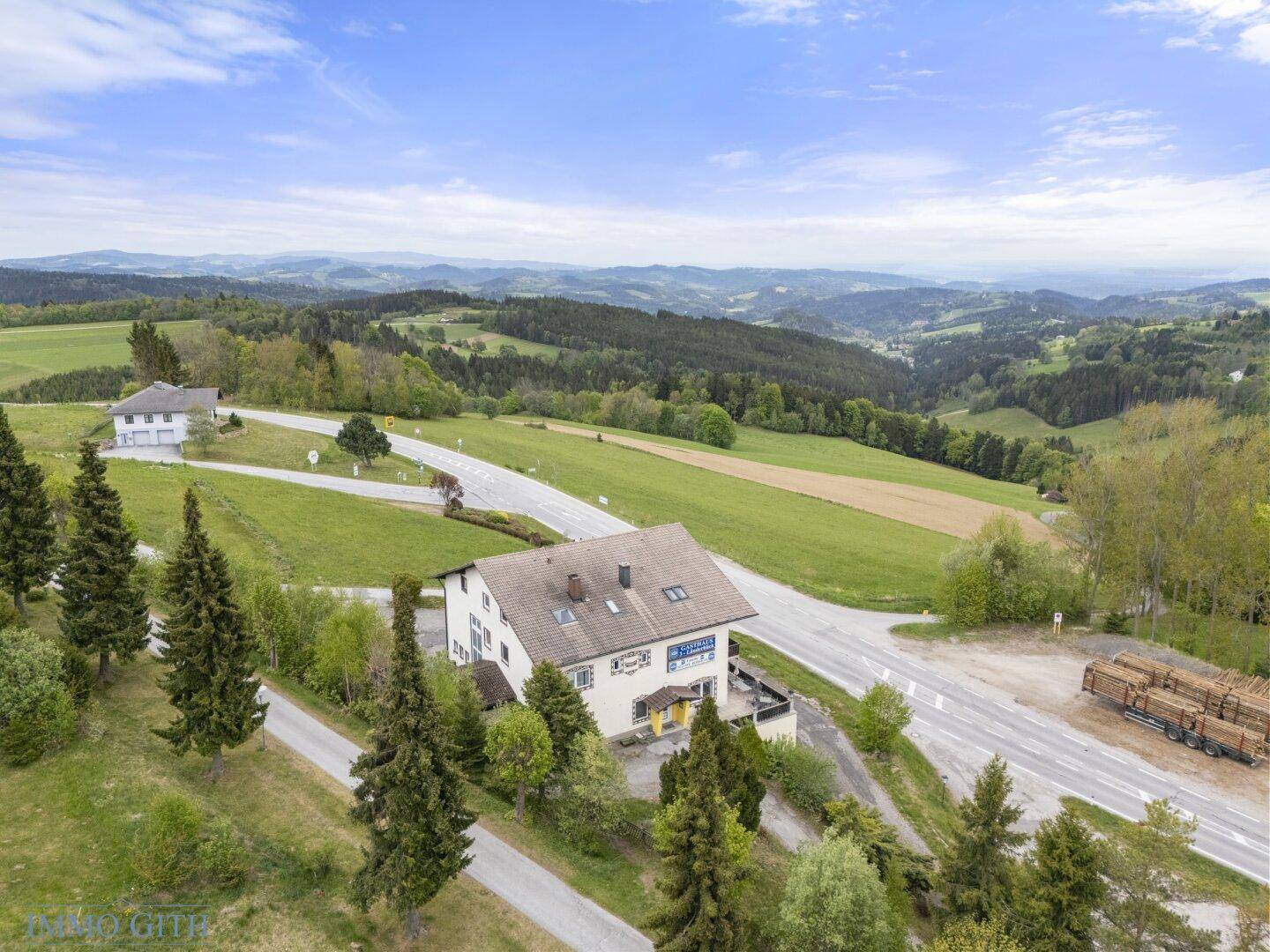 Luftaufnahme des Gasthauses in einer malerischen Hügellandschaft mit Wäldern und Straßen.