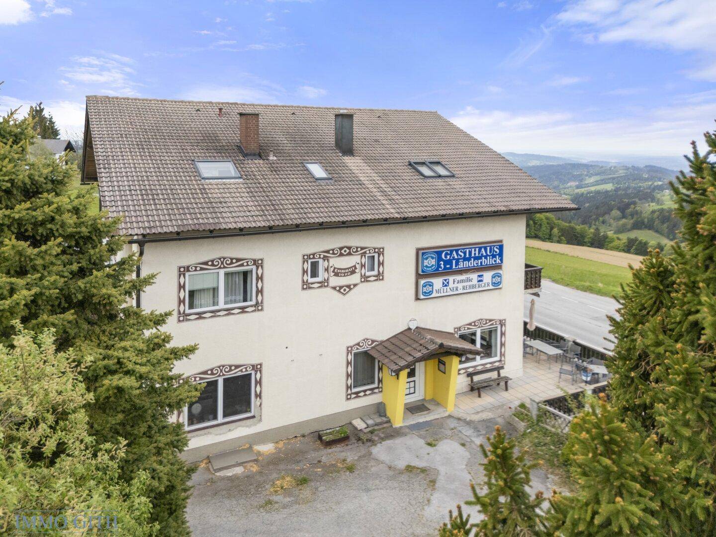 Vorderansicht des Gasthauses mit traditioneller Fassade, Dachfenstern und umgebenden Bäumen.