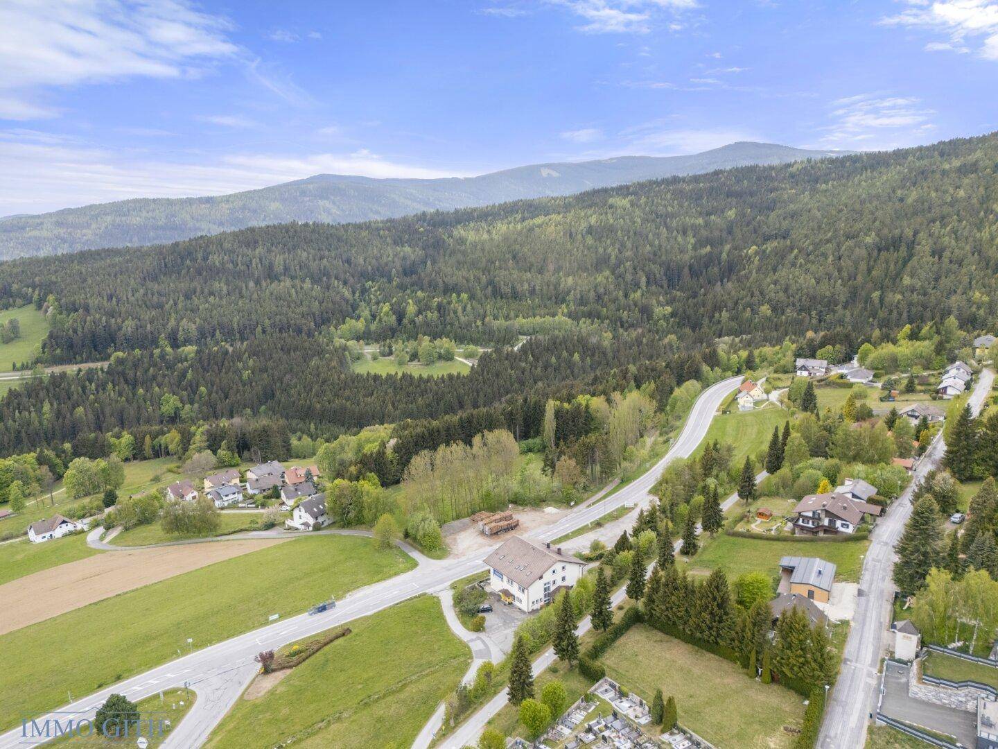 Weitläufige Landschaft mit dichten Wäldern, grünen Feldern und einer Straße, die sich durch die Hügel schlängelt.