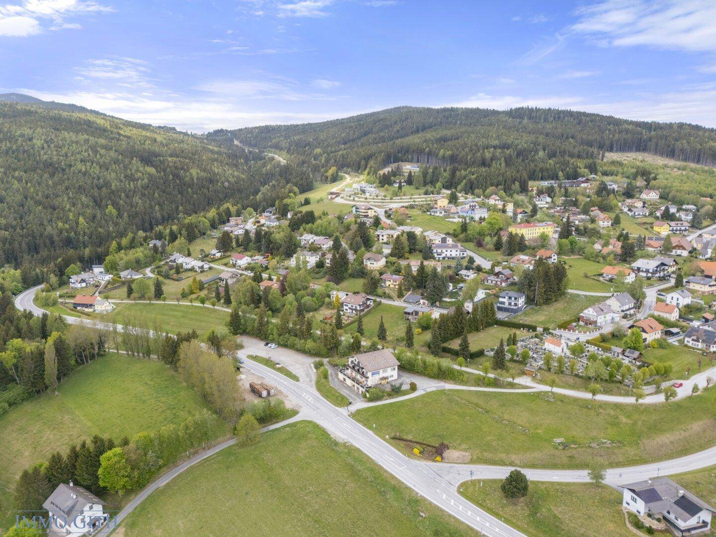 Panoramablick auf eine ländliche Siedlung mit Häusern, Straßen und weiten grünen Flächen.