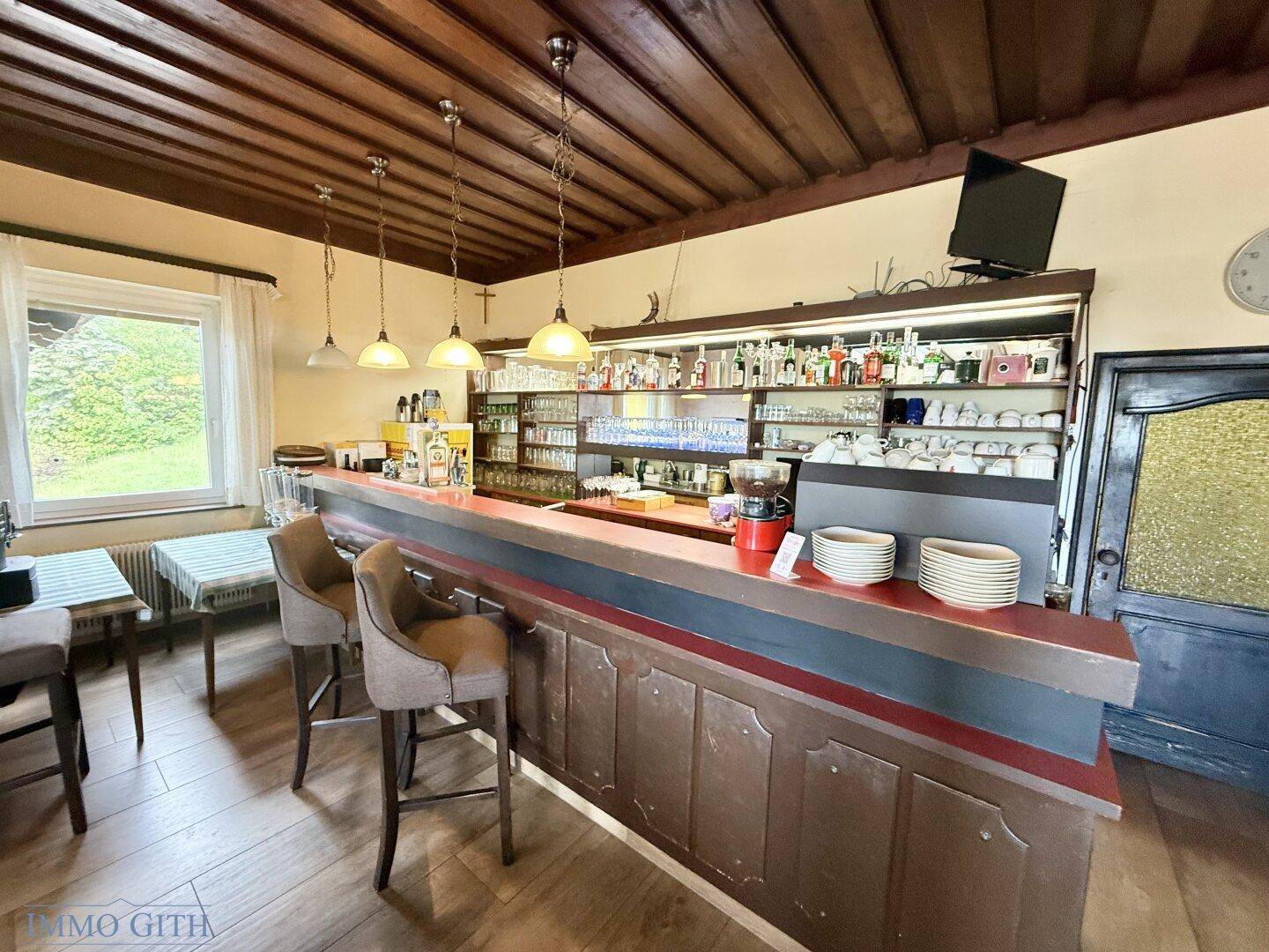 Gemütliche Bar mit Holztheke, Barhockern und einer großen Auswahl an Getränken.