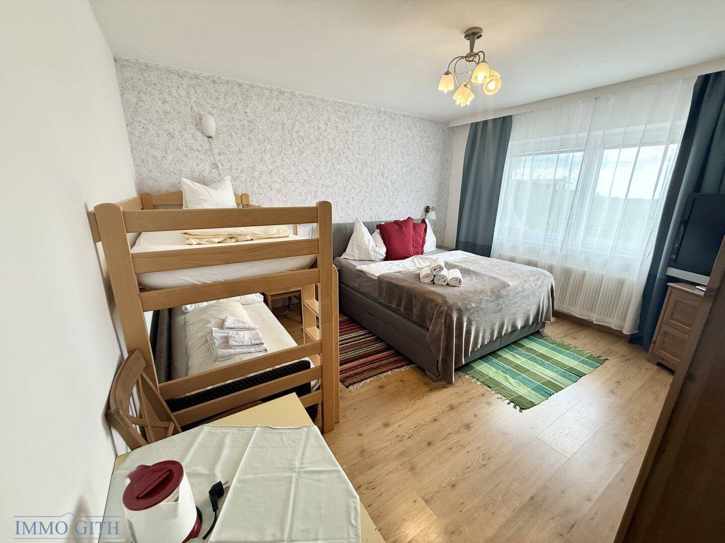 Schlafzimmer mit Doppelbett, Etagenbett und Holzboden, hell und freundlich eingerichtet.