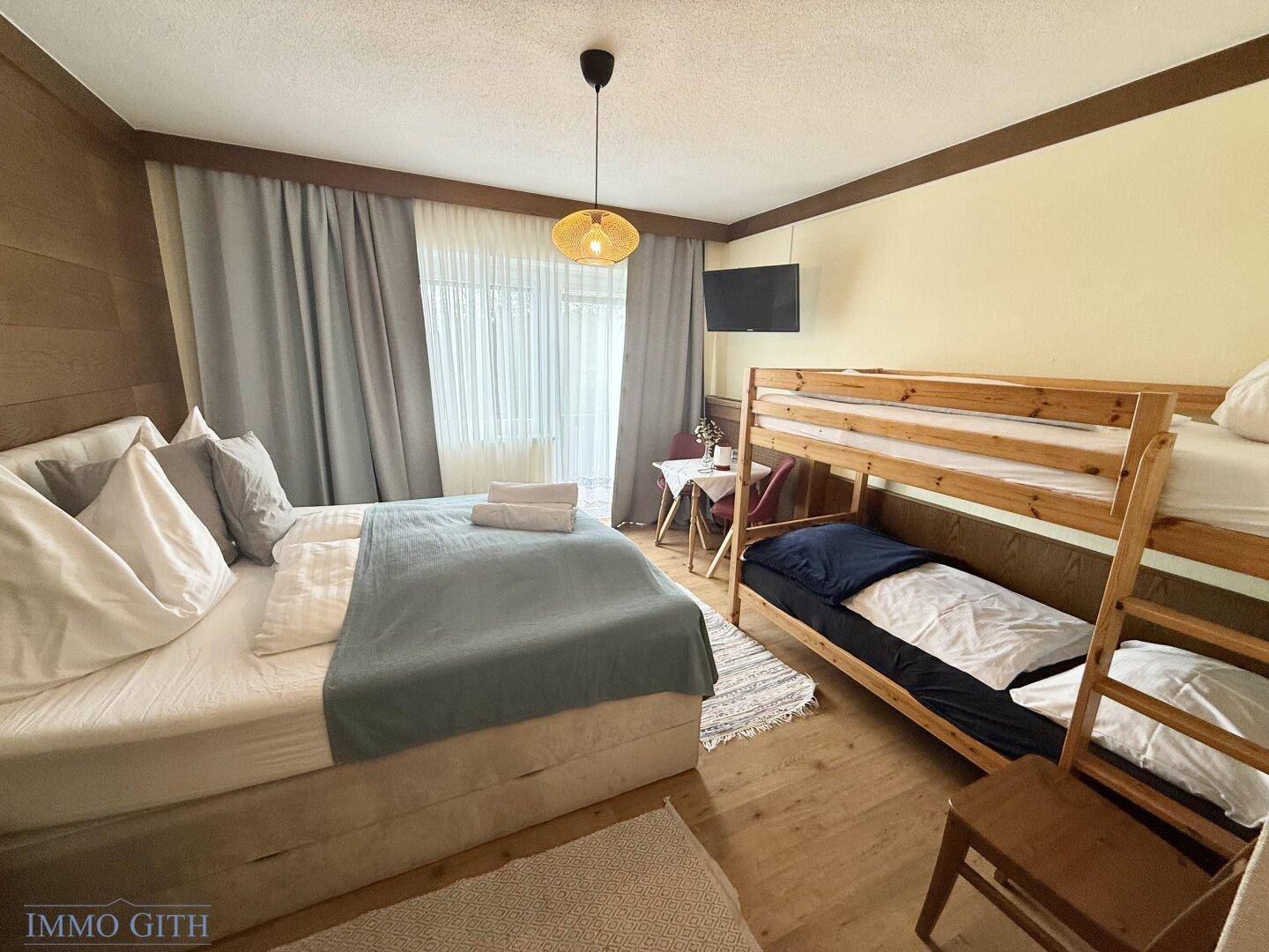 Schlafzimmer mit Doppelbett, Etagenbett und Holzwandverkleidung, gemütlich eingerichtet.