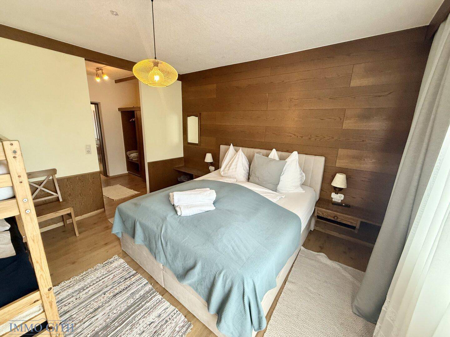 Schlafzimmer mit Doppelbett, Holzwandverkleidung und Nachttischen, hell und einladend.