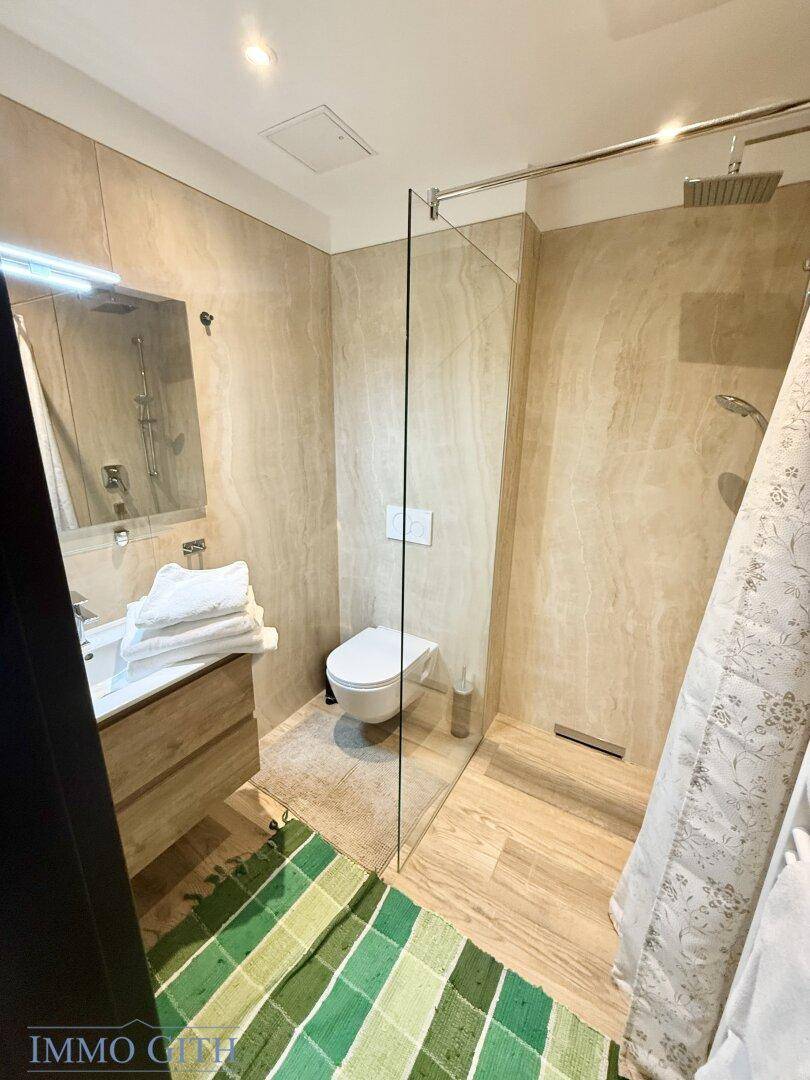 Modernes Badezimmer mit beigefarbenen Fliesen, bodengleicher Dusche und hölzernem Waschtischunterschrank.