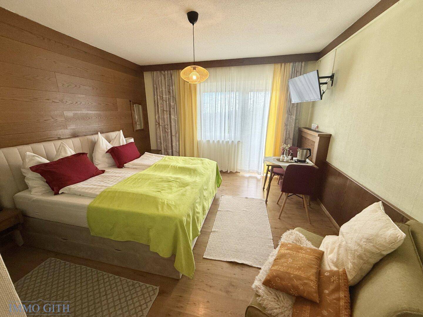 Gemütliches Schlafzimmer mit Doppelbett, Holzwänden und einem kleinen Essbereich am Fenster.