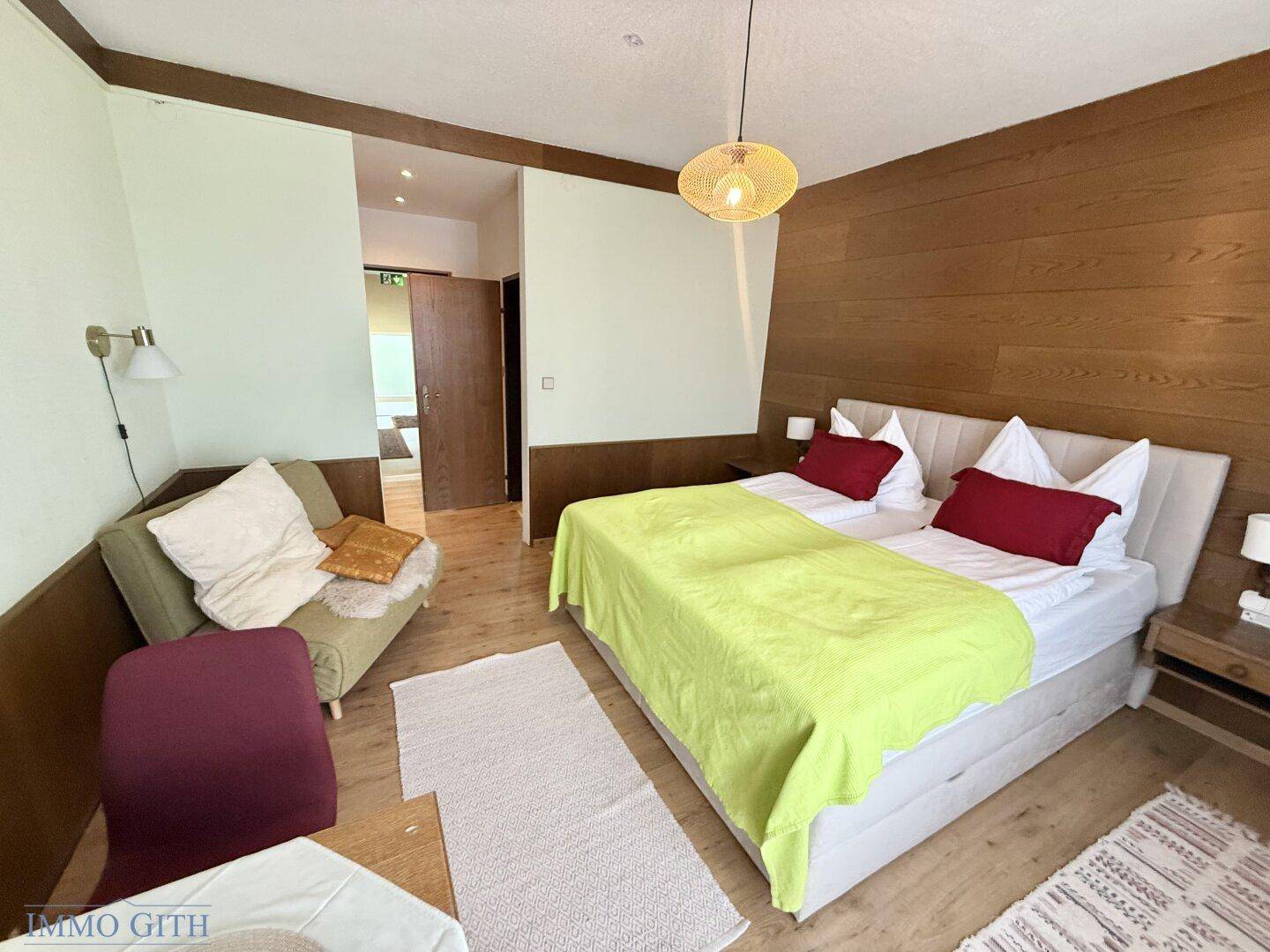 Geräumiges Schlafzimmer mit Holzwänden, Doppelbett und Zugang zu einem weiteren Raum.