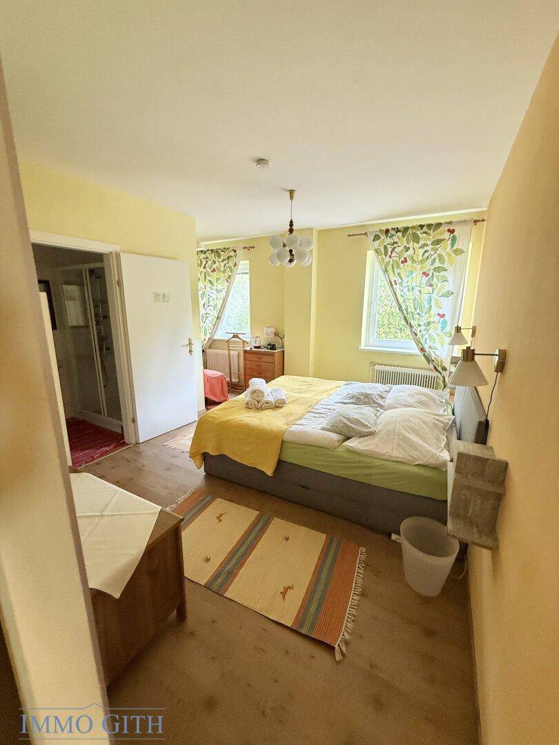 Helles Schlafzimmer mit gelben Wänden, Doppelbett und Zugang zu einem angrenzenden Badezimmer.