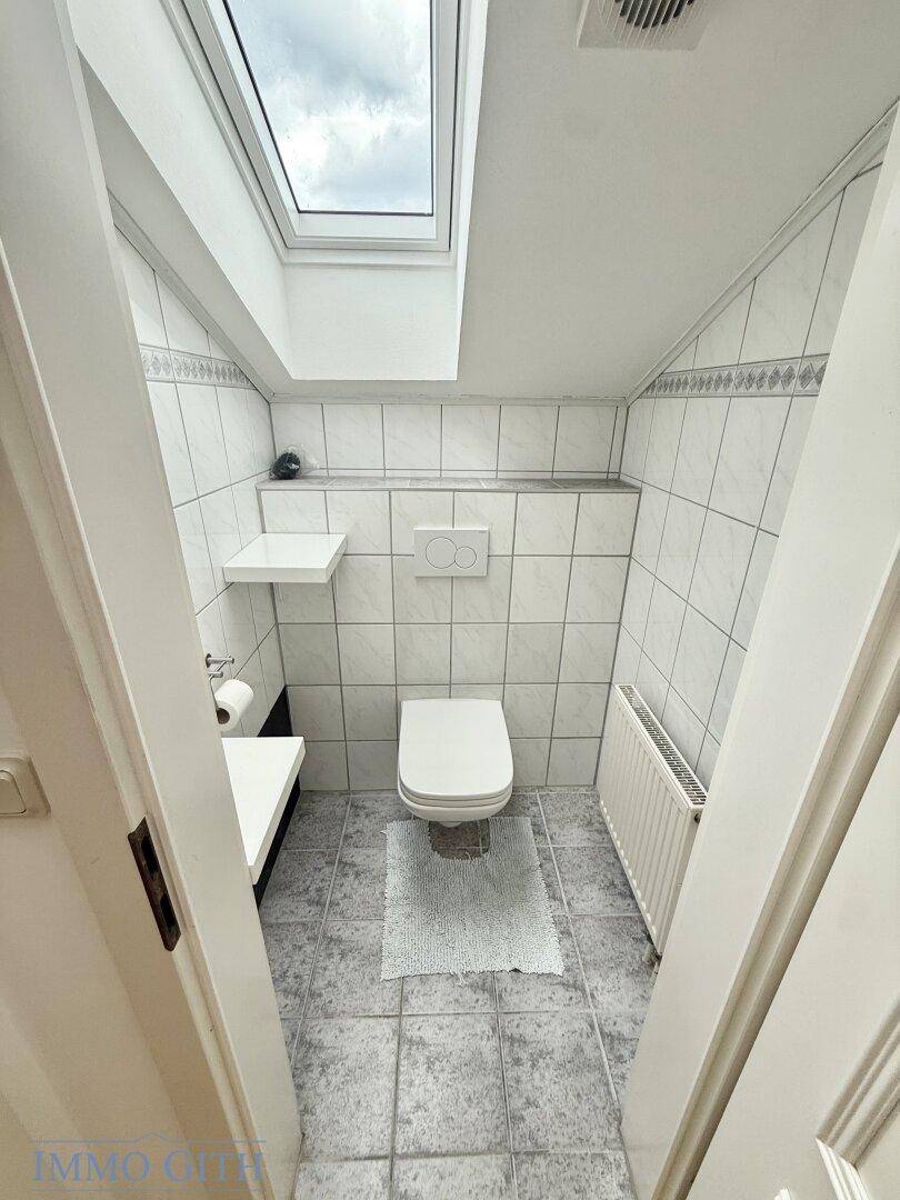 Kleines Gäste-WC mit Dachfenster, weißen Fliesen und Wand-WC.