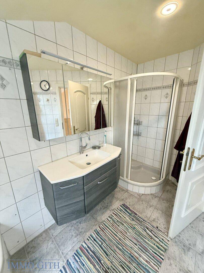 Badezimmer mit Duschkabine, Waschtischunterschrank und weißen Wandfliesen.