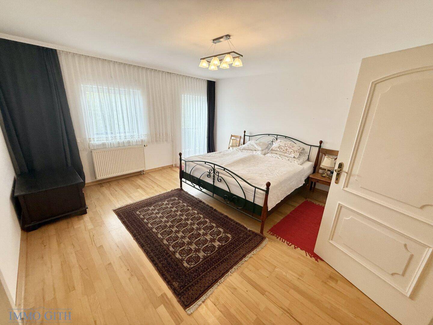 Helles Schlafzimmer mit Holzboden, schmiedeeisernem Bett und großem Fenster.