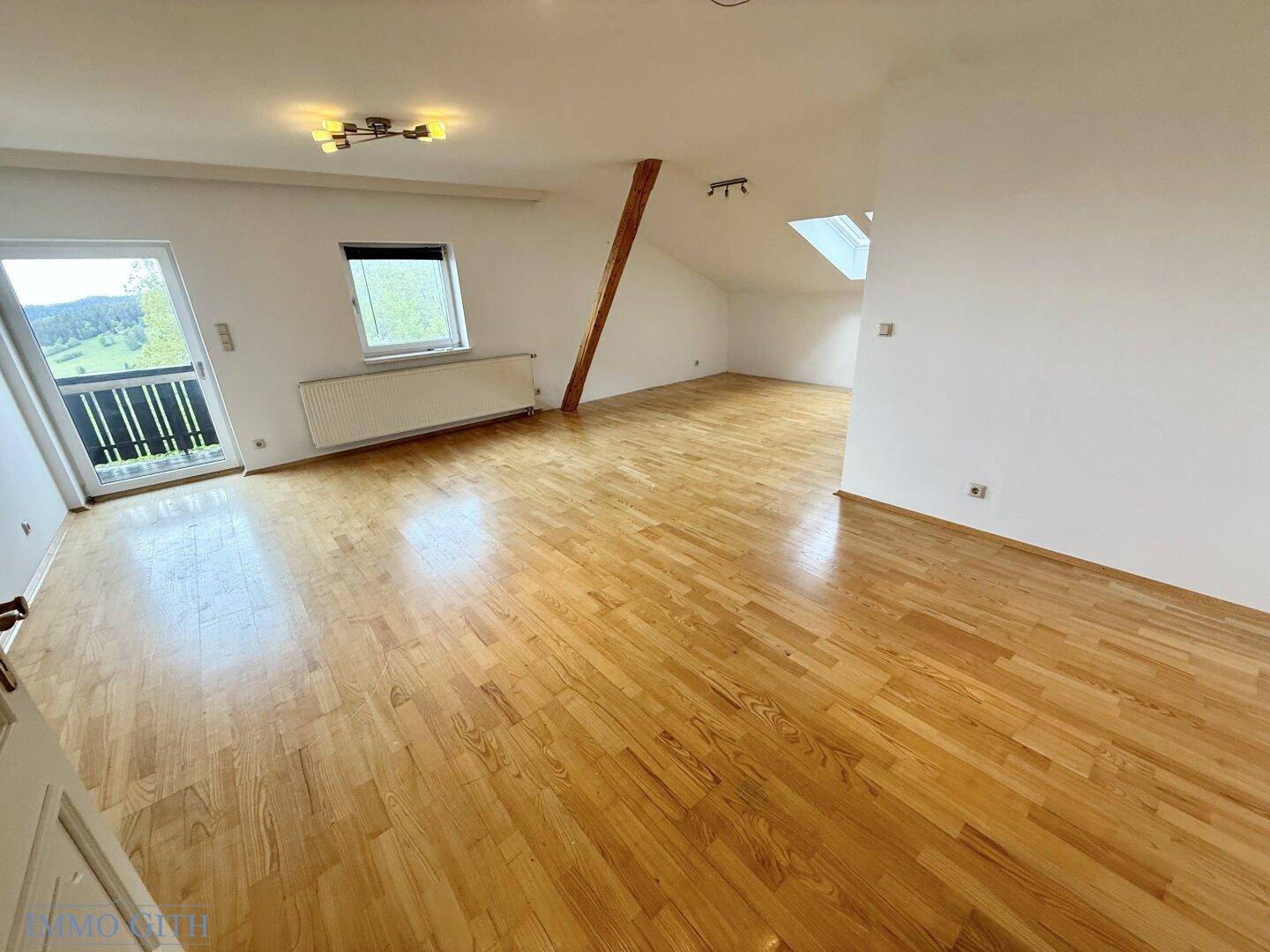 Großer, heller Wohnraum mit Holzboden, Dachschrägen und Zugang zum Balkon.