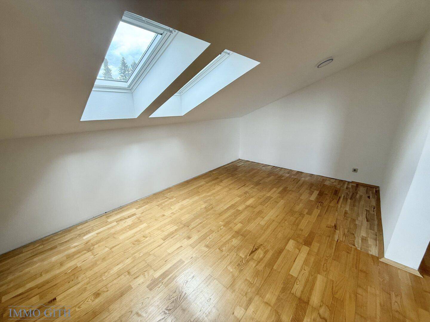 Schlafzimmer mit Holzboden, Dachschrägen und zwei Dachfenstern für viel Tageslicht.