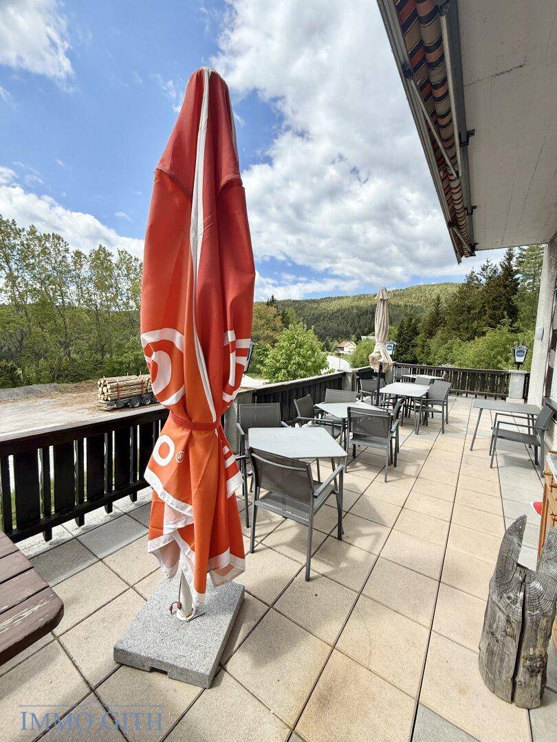 Außenterrasse mit Tischen und Stühlen, Sonnenschirmen und Blick auf die grüne Umgebung.
