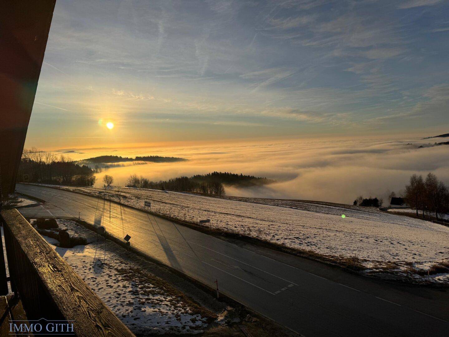 Malerischer Sonnenuntergang über einer Nebeldecke, die sich über die Landschaft legt.